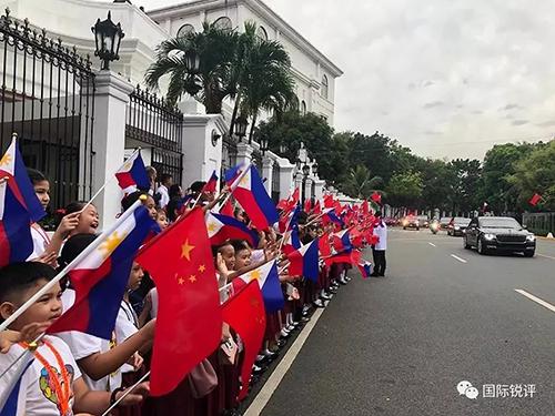 20日，來自馬尼拉當地三所小學的千名小學生站在總統府道路兩側揮舞兩國國旗，歡迎習主席車隊。（圖片來源：中央廣播電視總臺央視新聞 記者鄧雪梅拍攝）